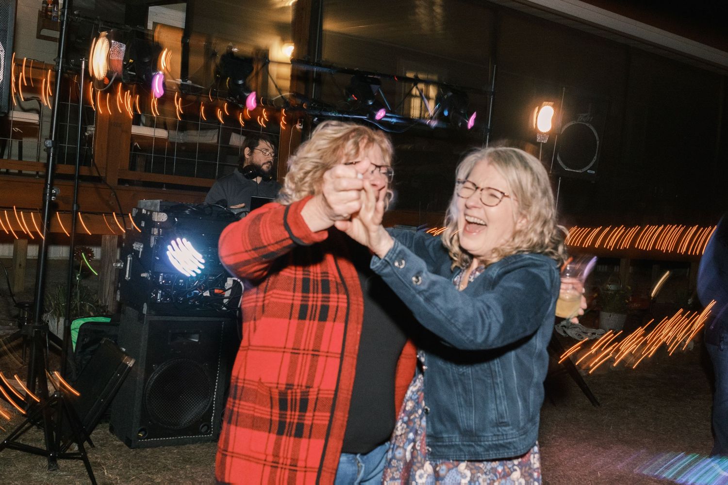 Two women laughing and dancing together joyfully at an indoor wedding reception celebration.