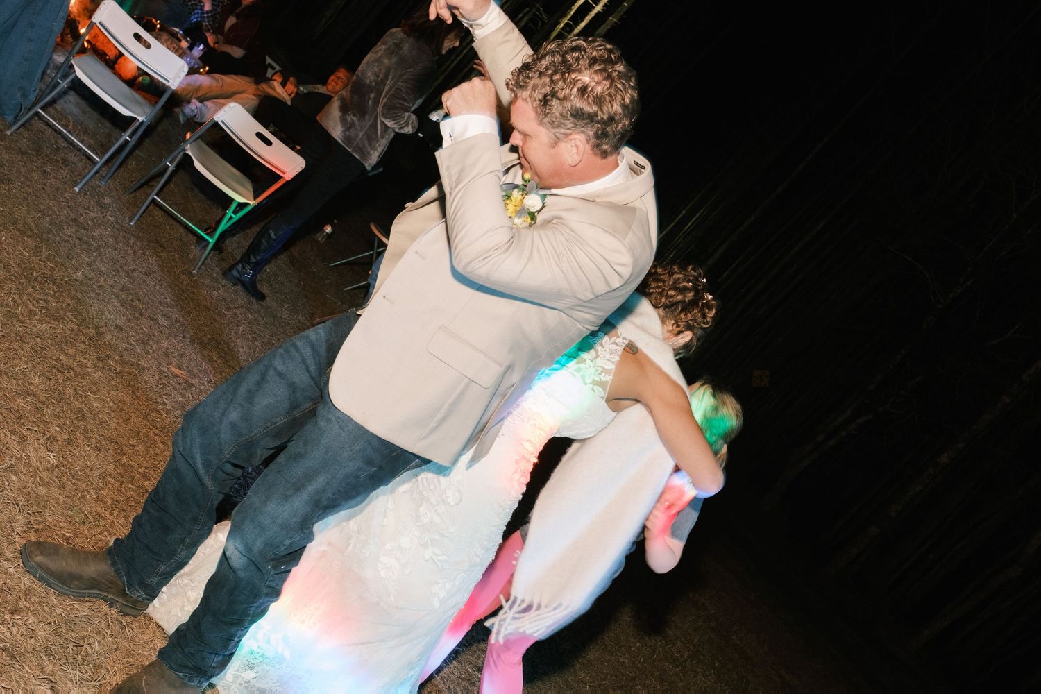 Groom in a tan suit dipping his bride in a white gown during a lively wedding reception dance.