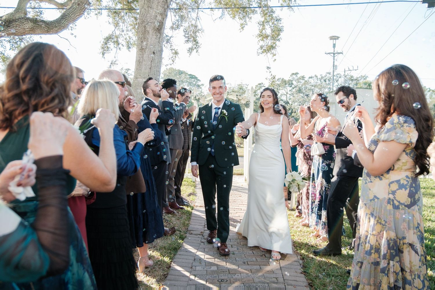 Wedding guests throwing confetti and celebrating outside under trees at a daytime celebration.