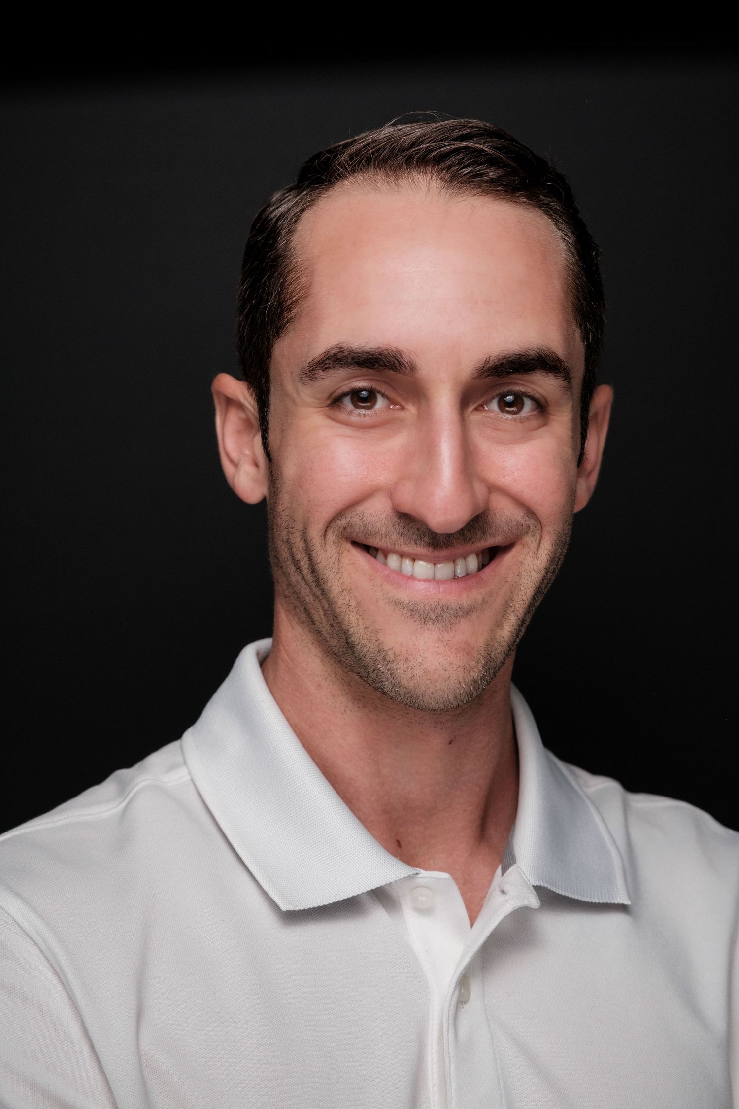 Professional headshot of a man in a white polo shirt against a dark background.