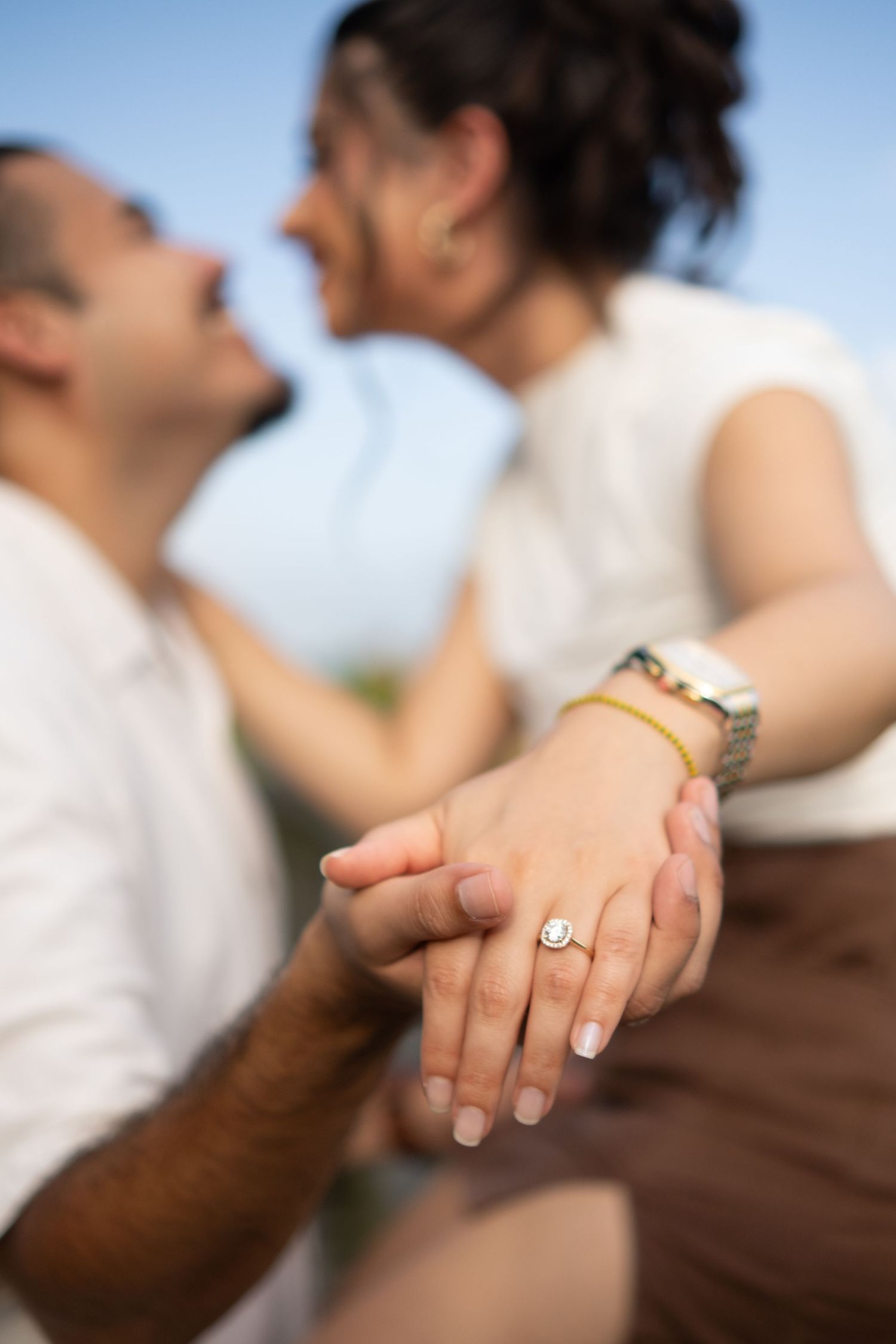 Close-up shot of hands with engagement ring against blurred background of an intimate moment.