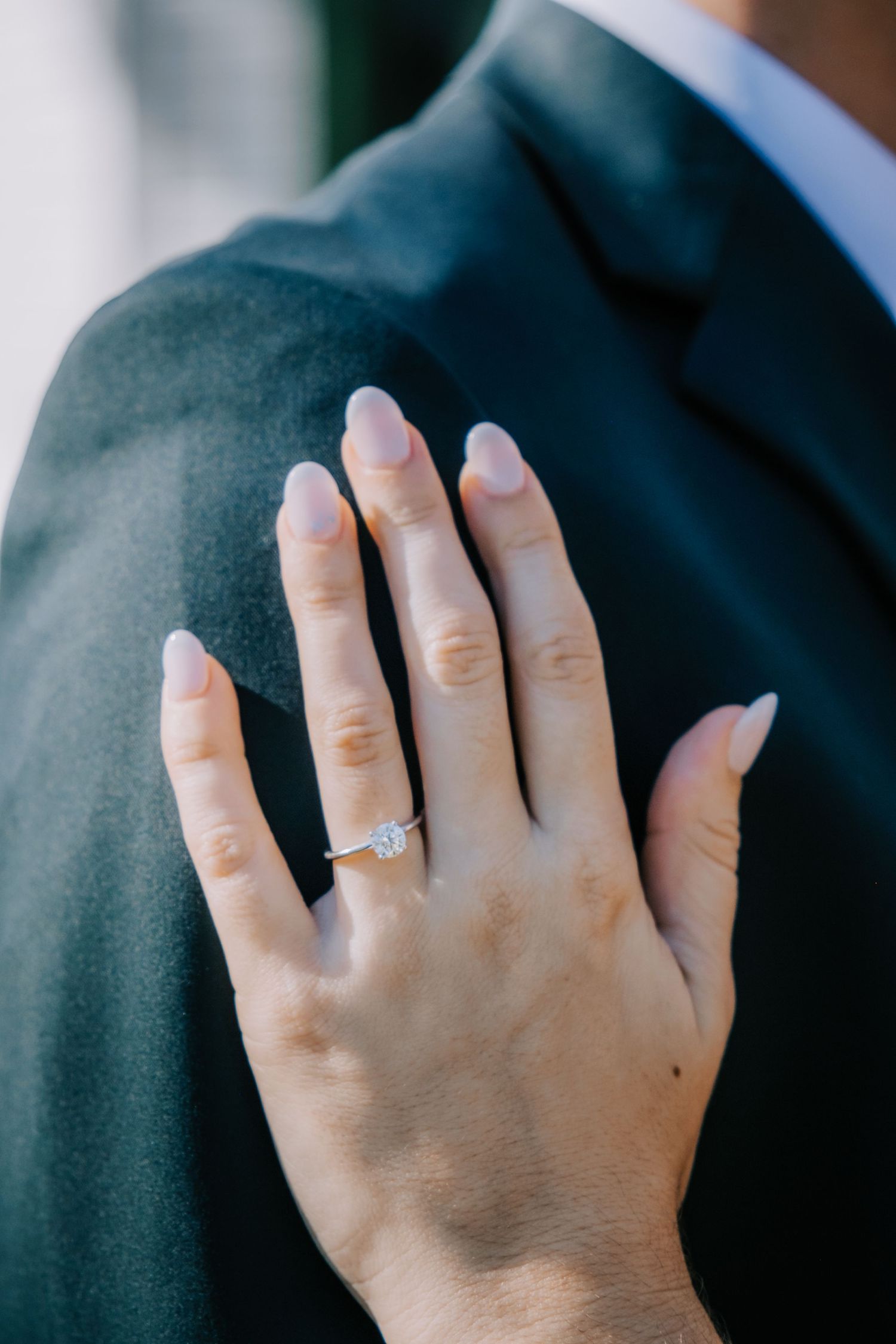 Close-up shots of hands showing off an elegant engagement ring against a dark suit.