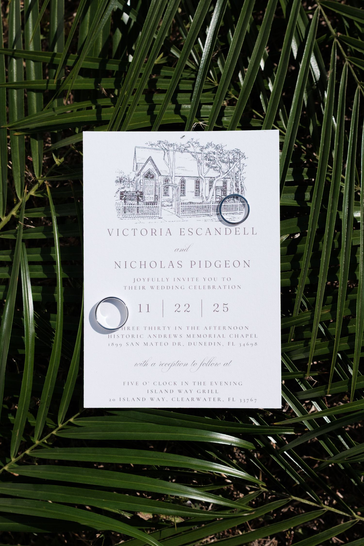 Elegant wedding invitations displayed on palm fronds with classic typography and minimalist design.