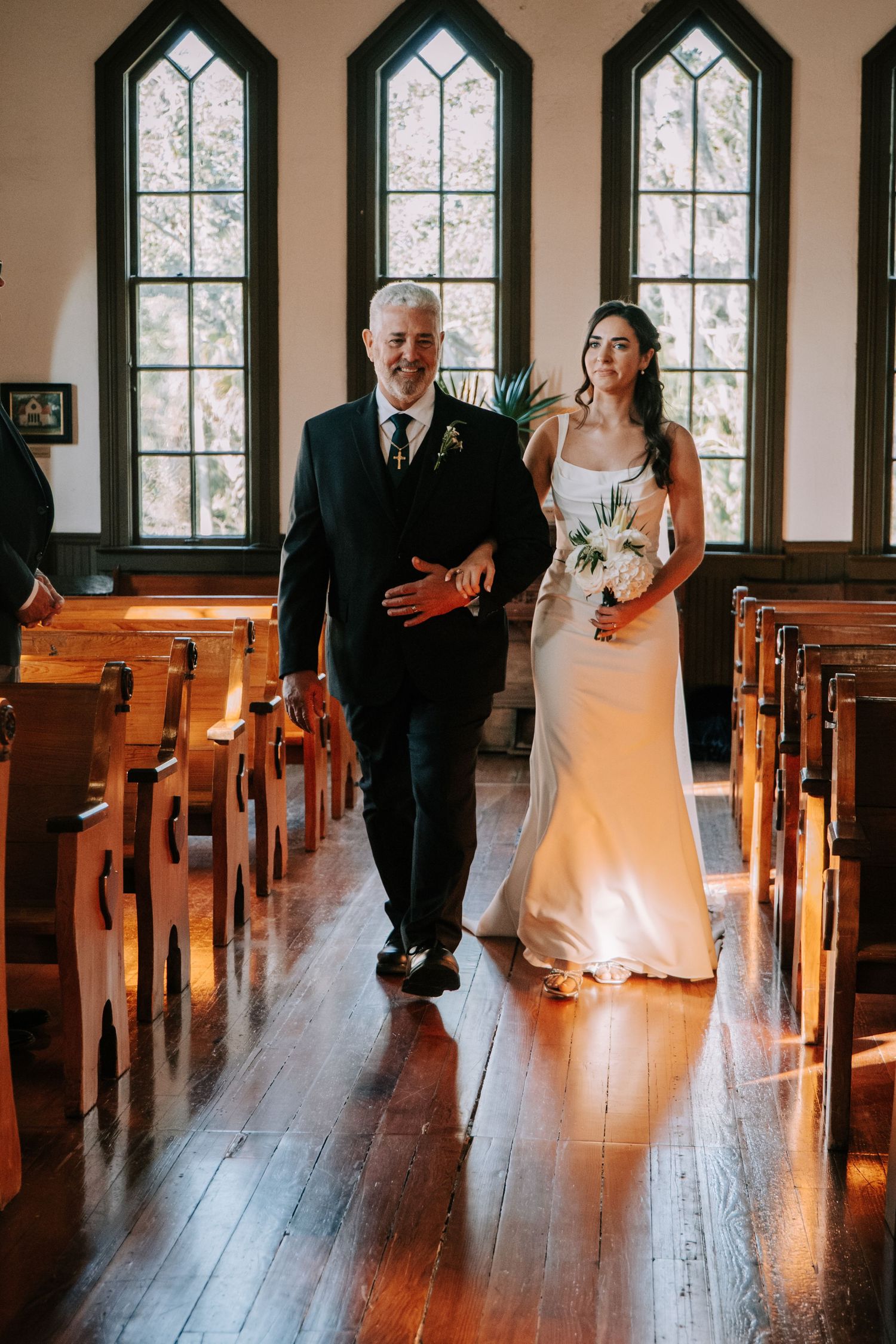 A wedding ceremony in a historic chapel with gothic arched windows and wooden pews.