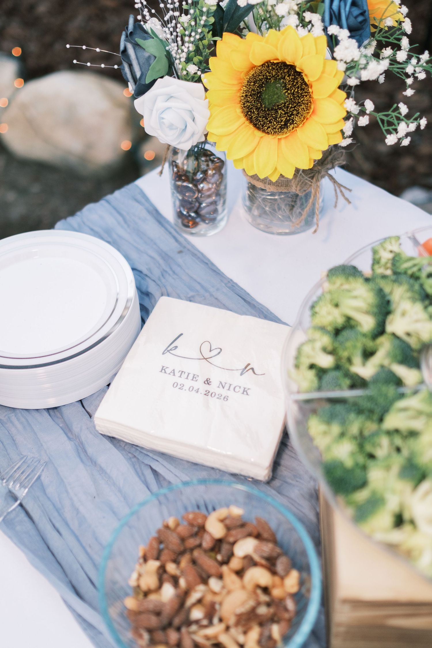 Wedding reception table with personalized Katie and Nick napkins, sunflower centerpiece, and fresh food spread.