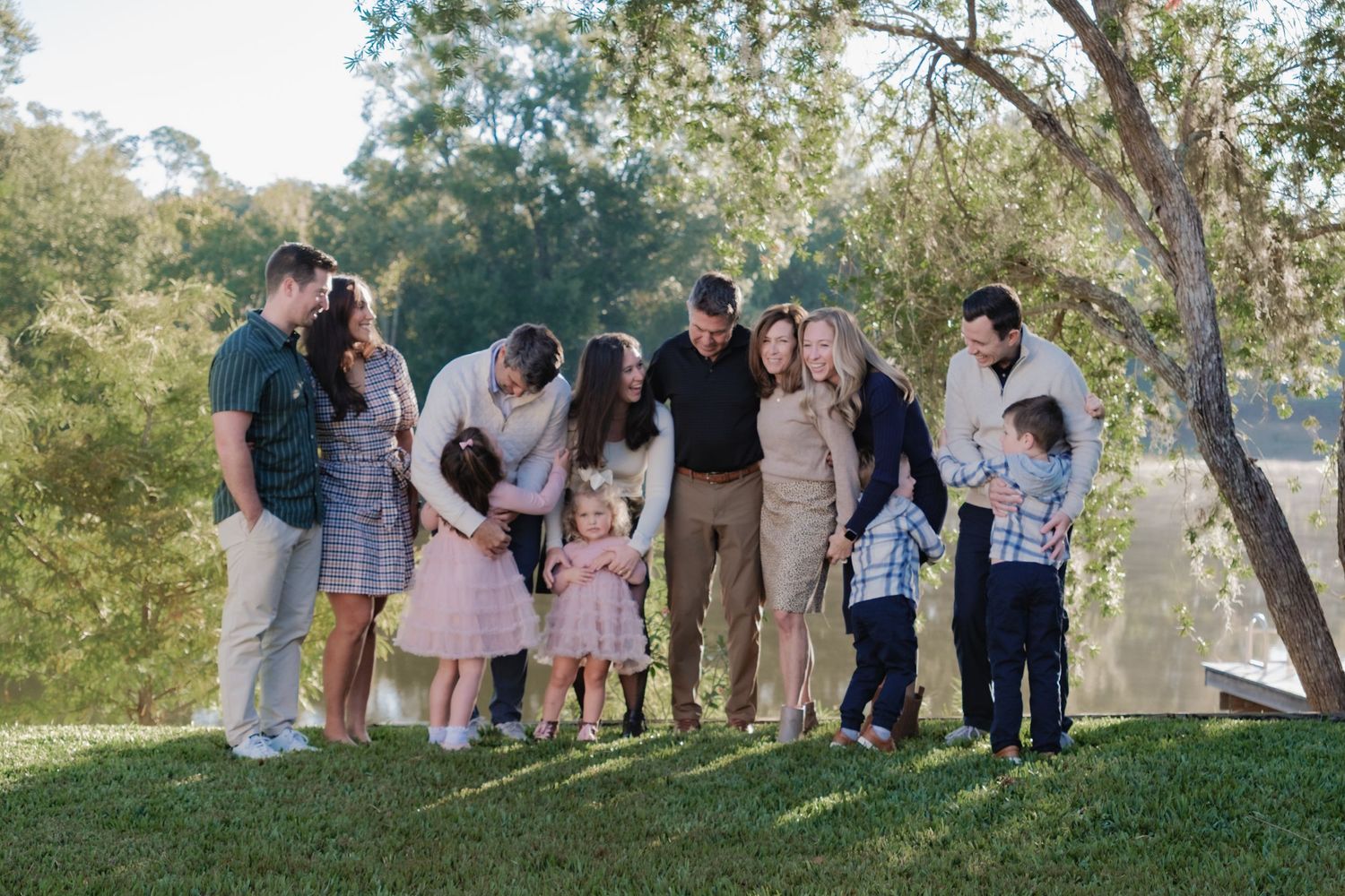 Large group in casual attire poses together on grassy hill during outdoor photo session at sunset.