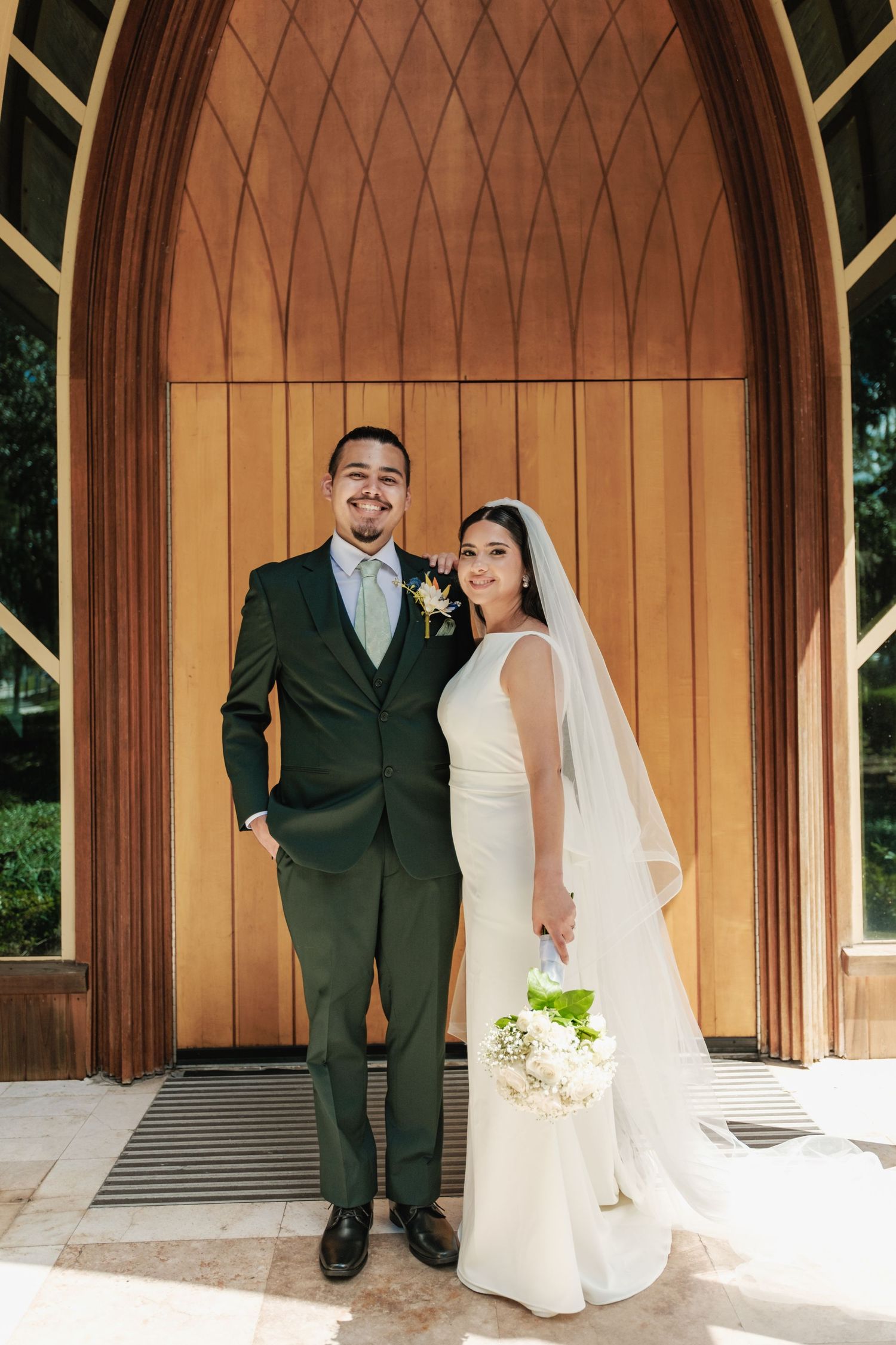 Wedding couple poses in front of a wooden chapel entrance with architectural details.