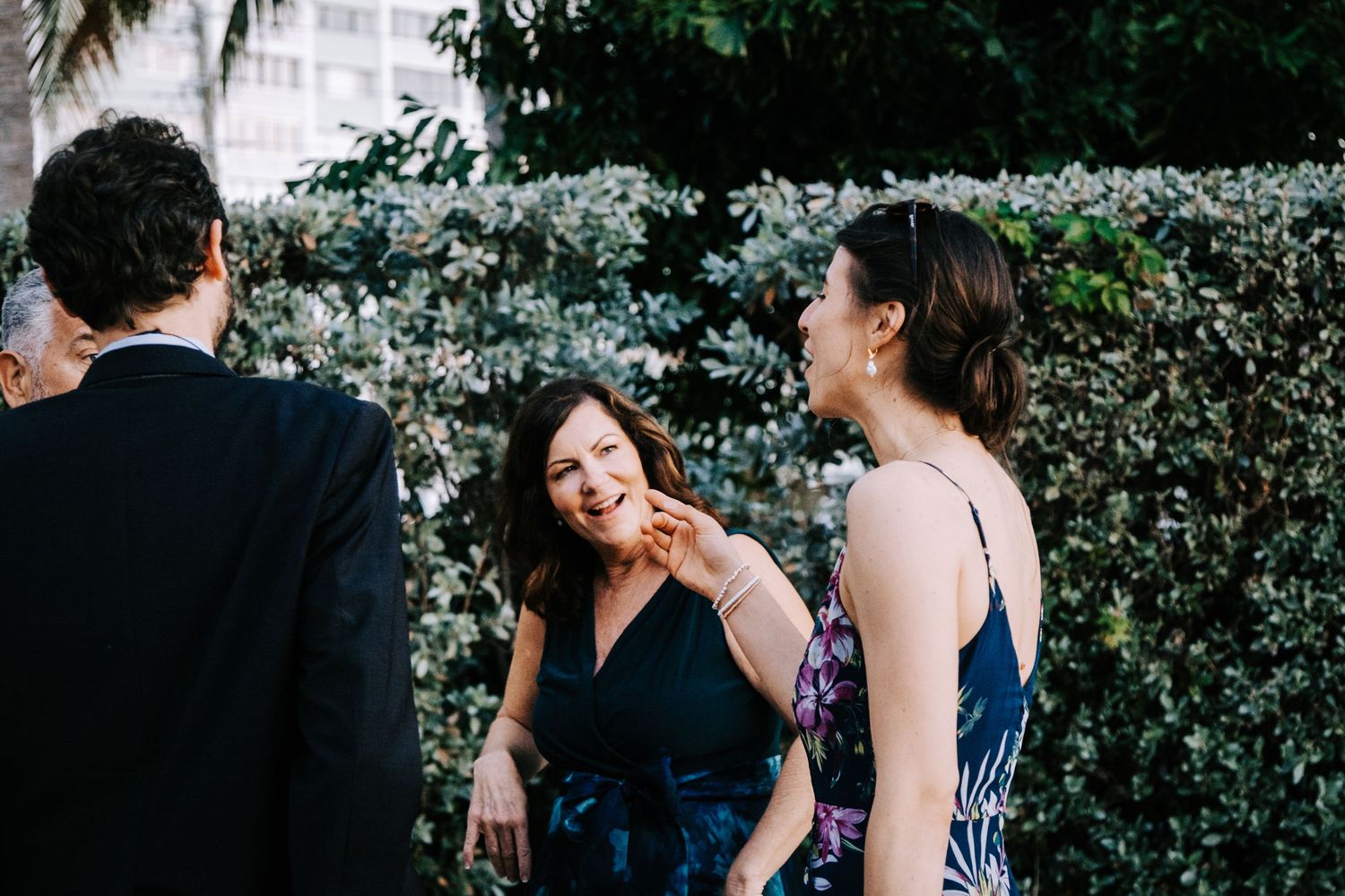 Wedding guests mingle during outdoor reception among lush greenery.