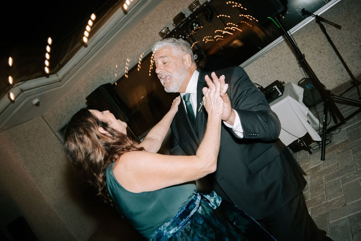 A couple dances together at a wedding reception, with the woman in a teal dress and the man in dark formal attire.