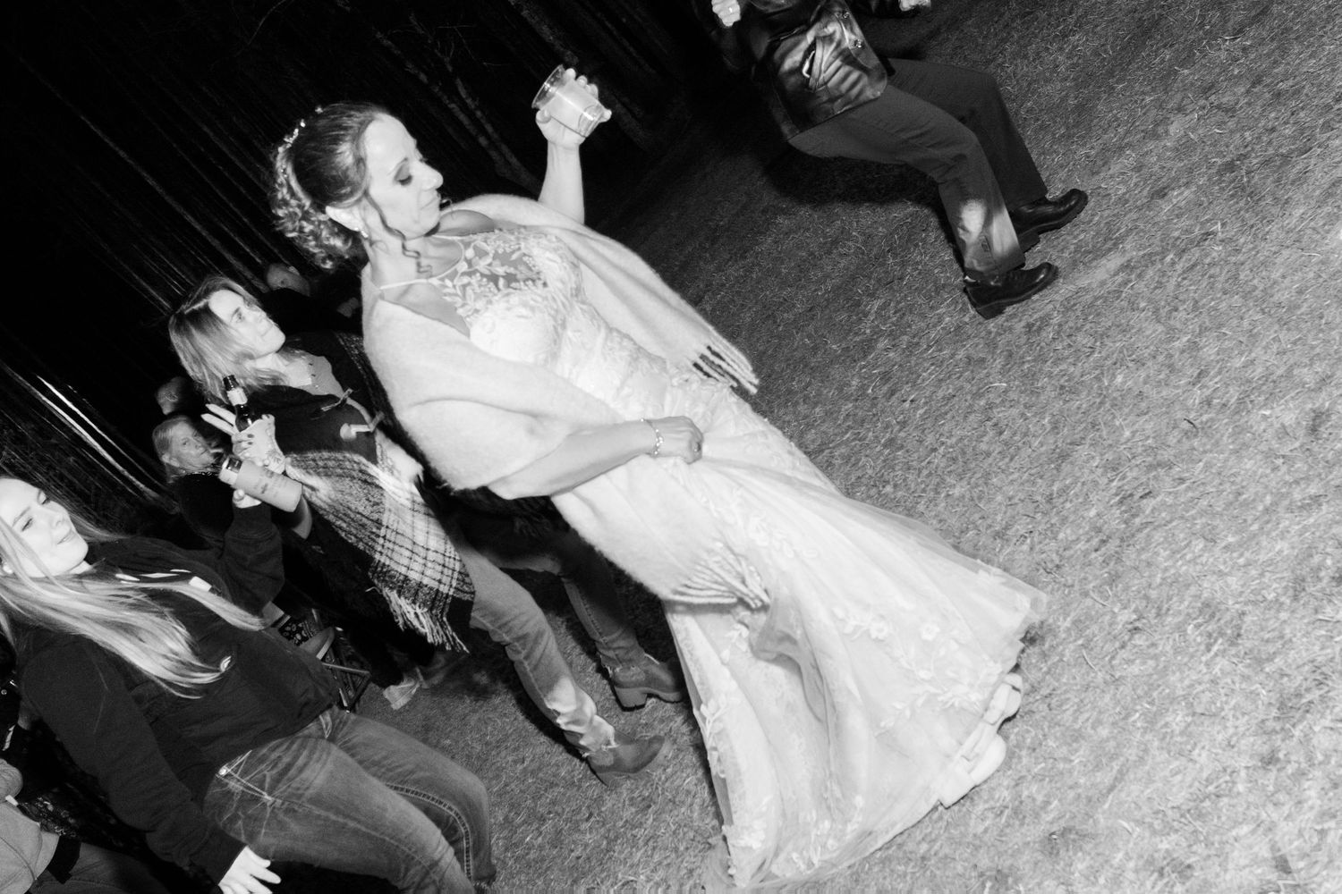 Black and white photo of bride and groom dancing at wedding reception with guests watching.