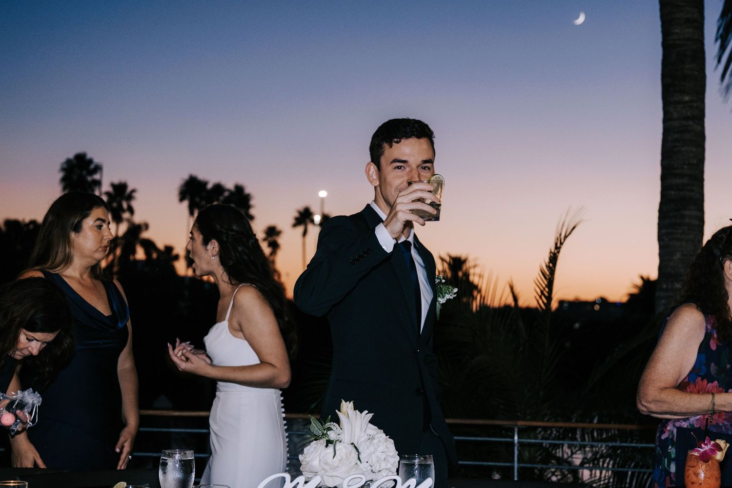 Wedding celebration silhouettes against dramatic sunset sky with palm trees.
