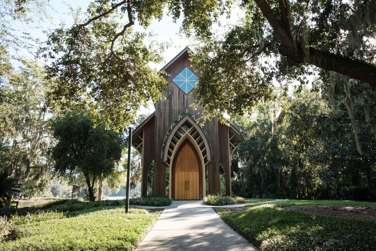 Rustic wooden chapel with arched doorway nestled among trees with a peaceful pathway leading to entrance.