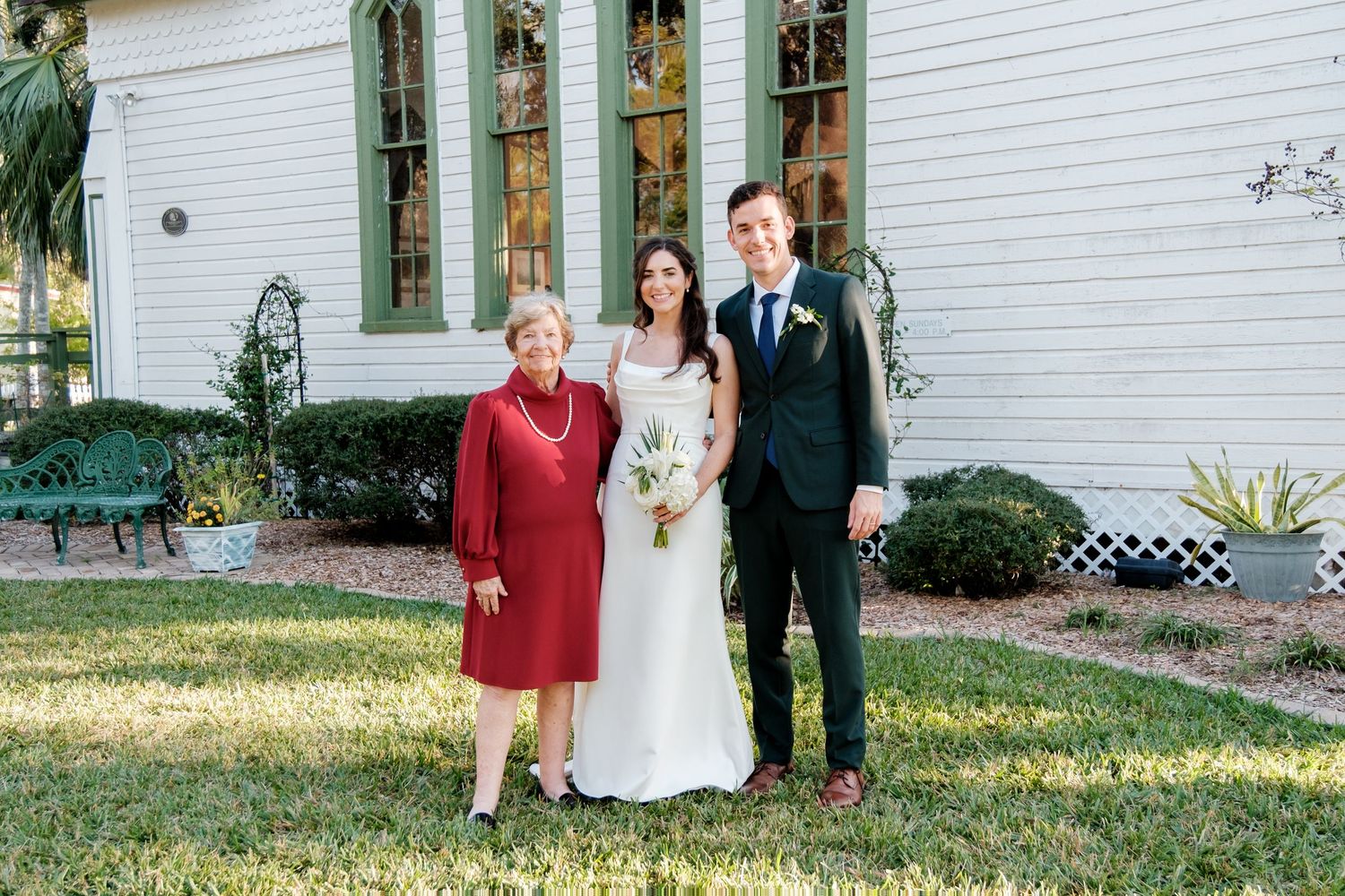 Wedding party poses for formal portrait outside white church.