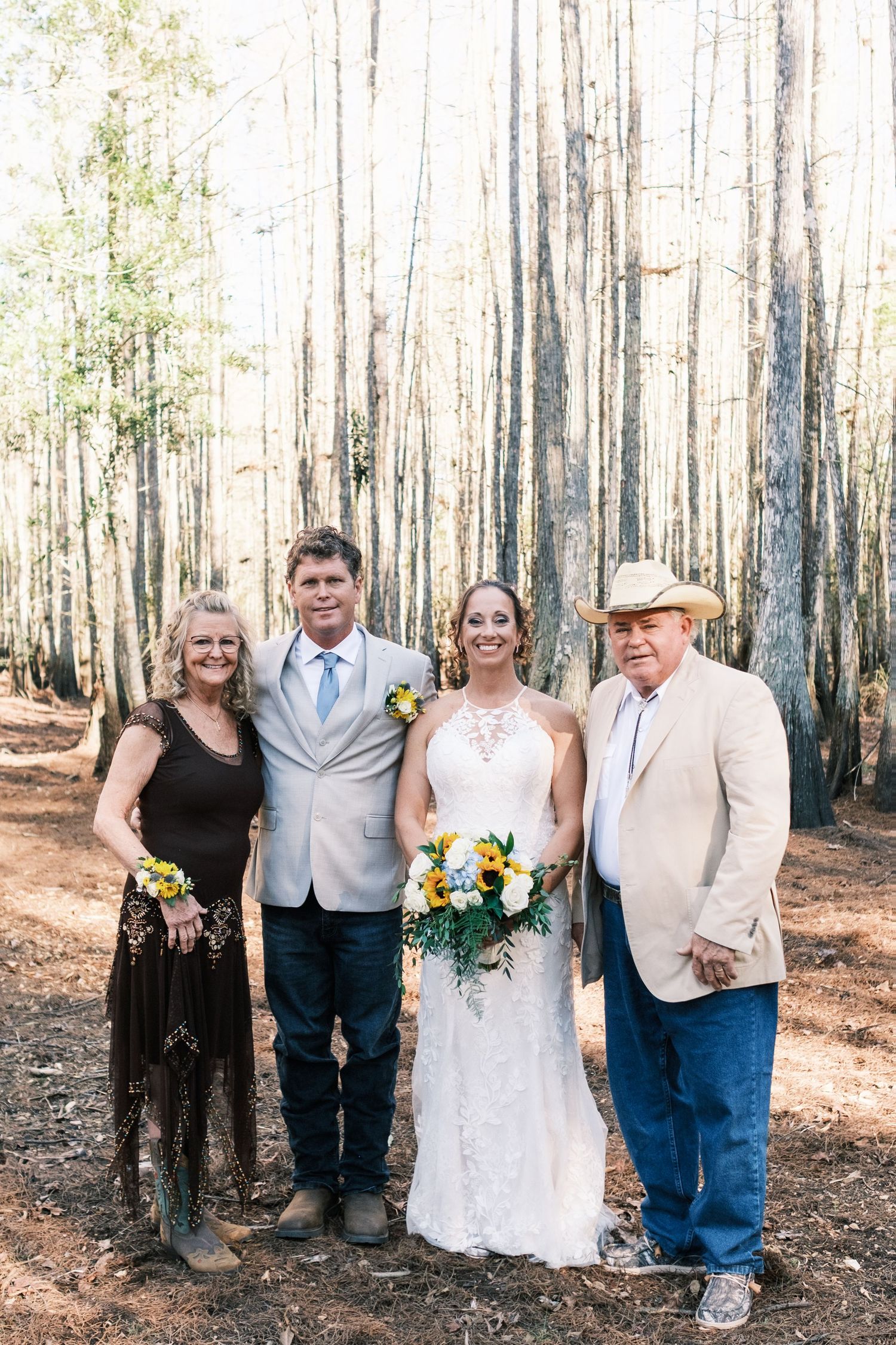 Bride and groom with two family members smile together in a forest setting with tall pine trees in the background.