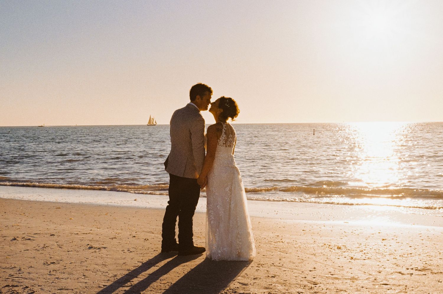 A bride and groom share a romantic kiss on the beach during a golden sunset wedding.