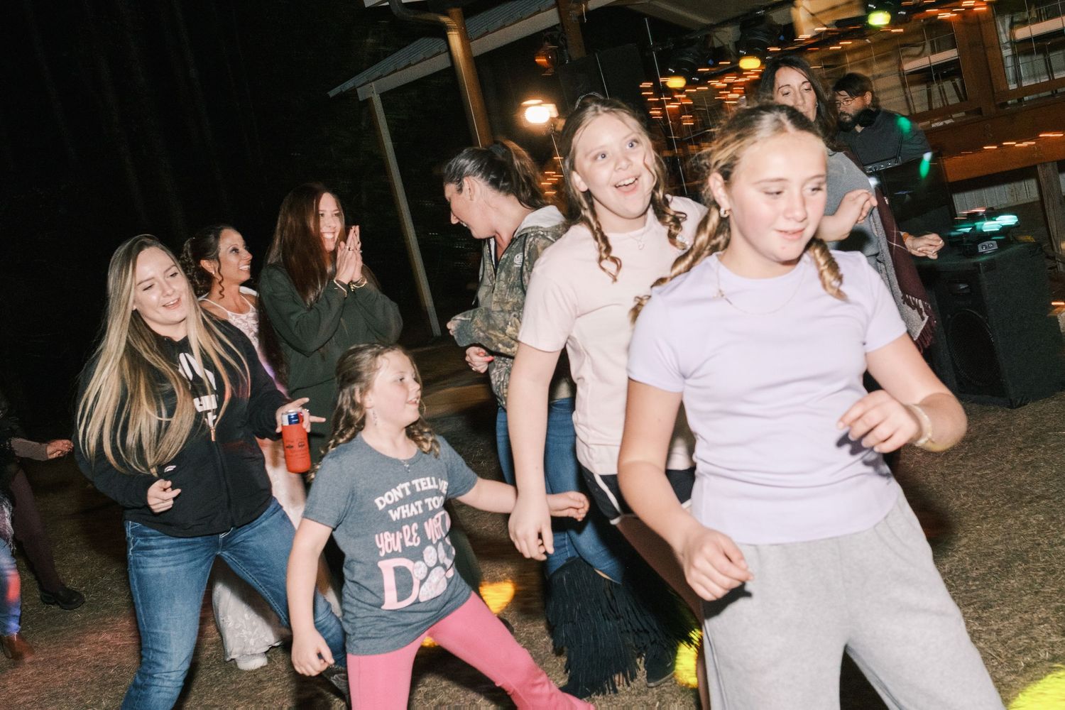 Group of children and guests dancing energetically on the dance floor at an outdoor evening wedding reception.