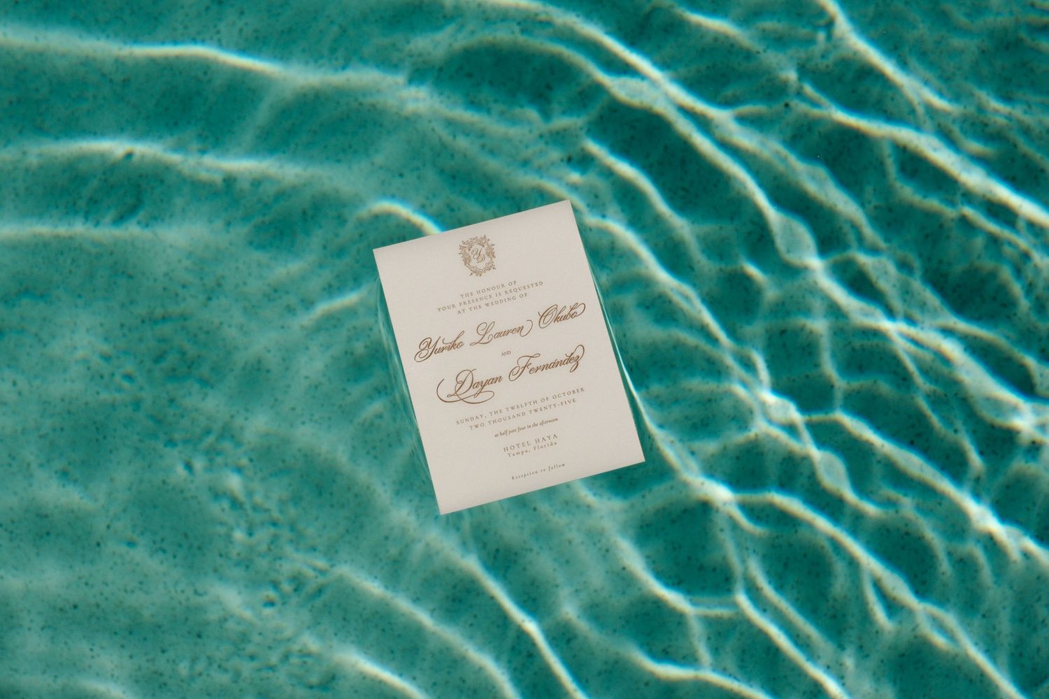 Wedding invitation floating on rippling turquoise pool water.