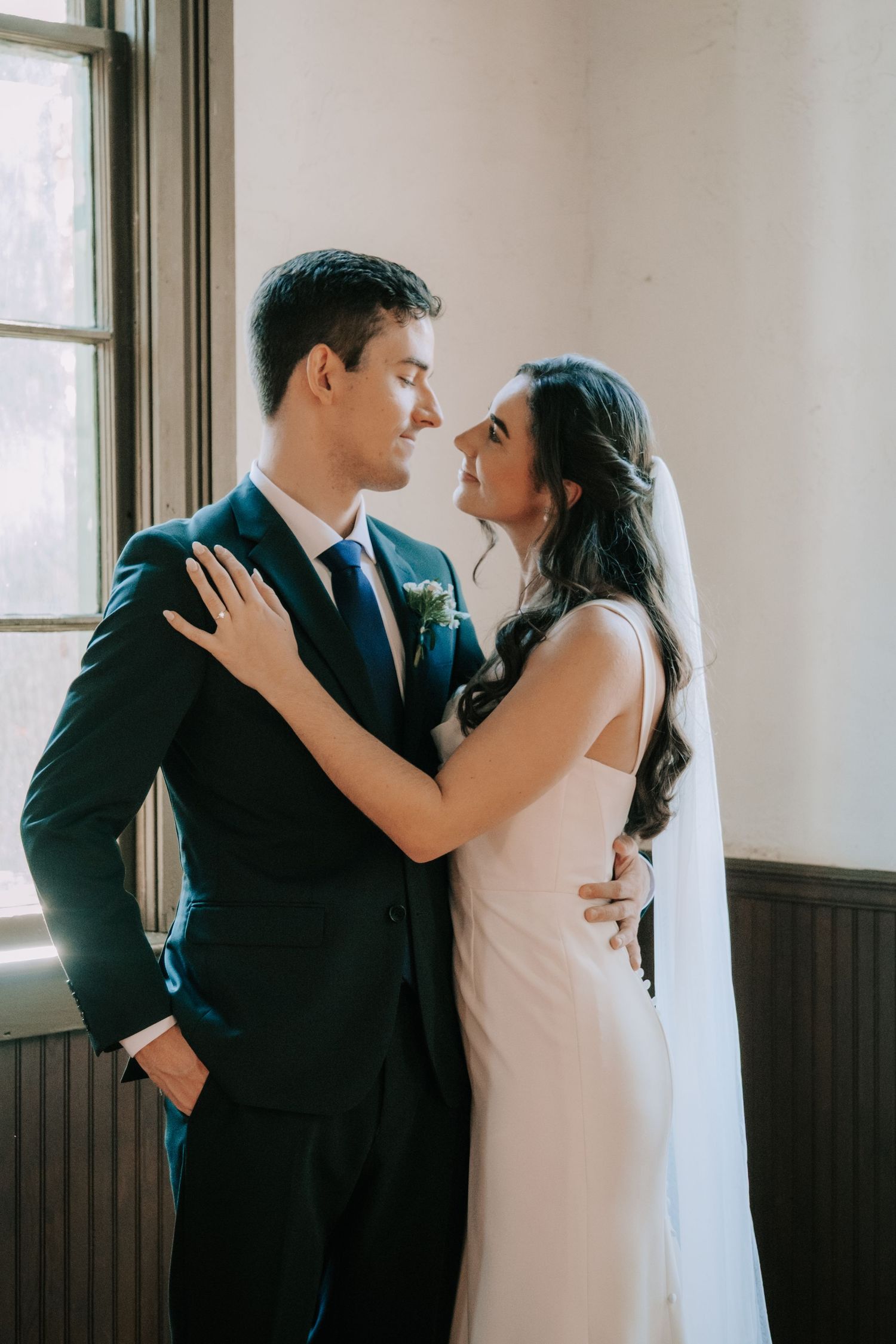 Tender moments between newlyweds in a light-filled room with white walls and wooden wainscoting.