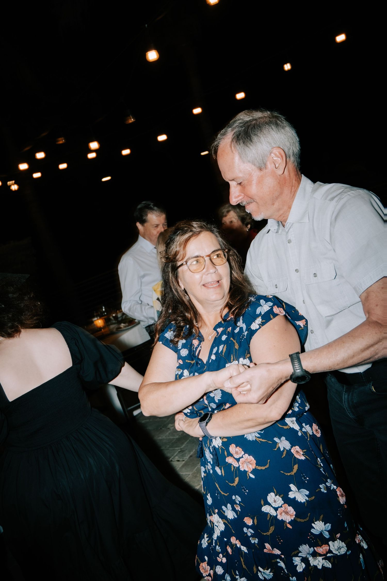 Couples dancing together at a wedding reception under ambient lighting.