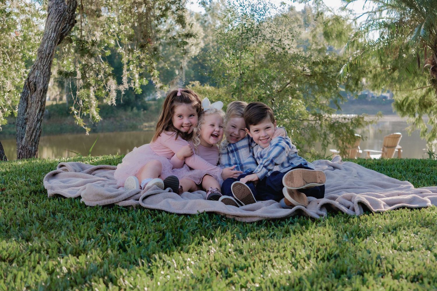 People enjoying a relaxing afternoon picnic on a blanket under trees near a lake.