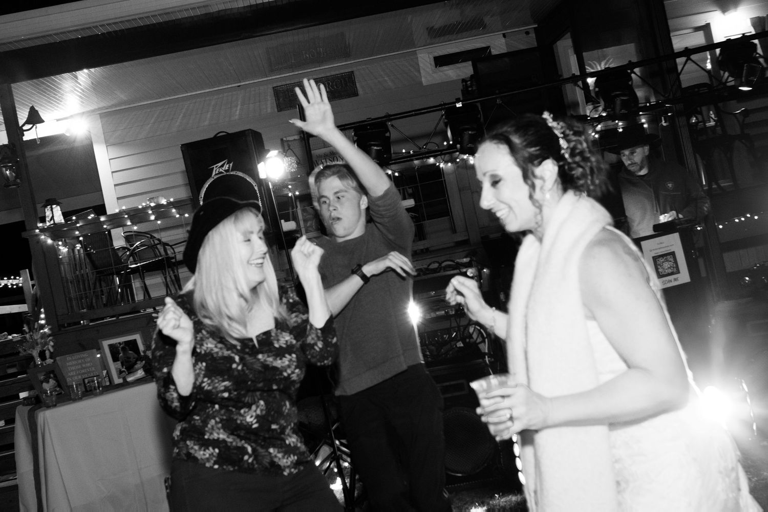 Black and white photo of guests dancing and celebrating at an indoor wedding reception.