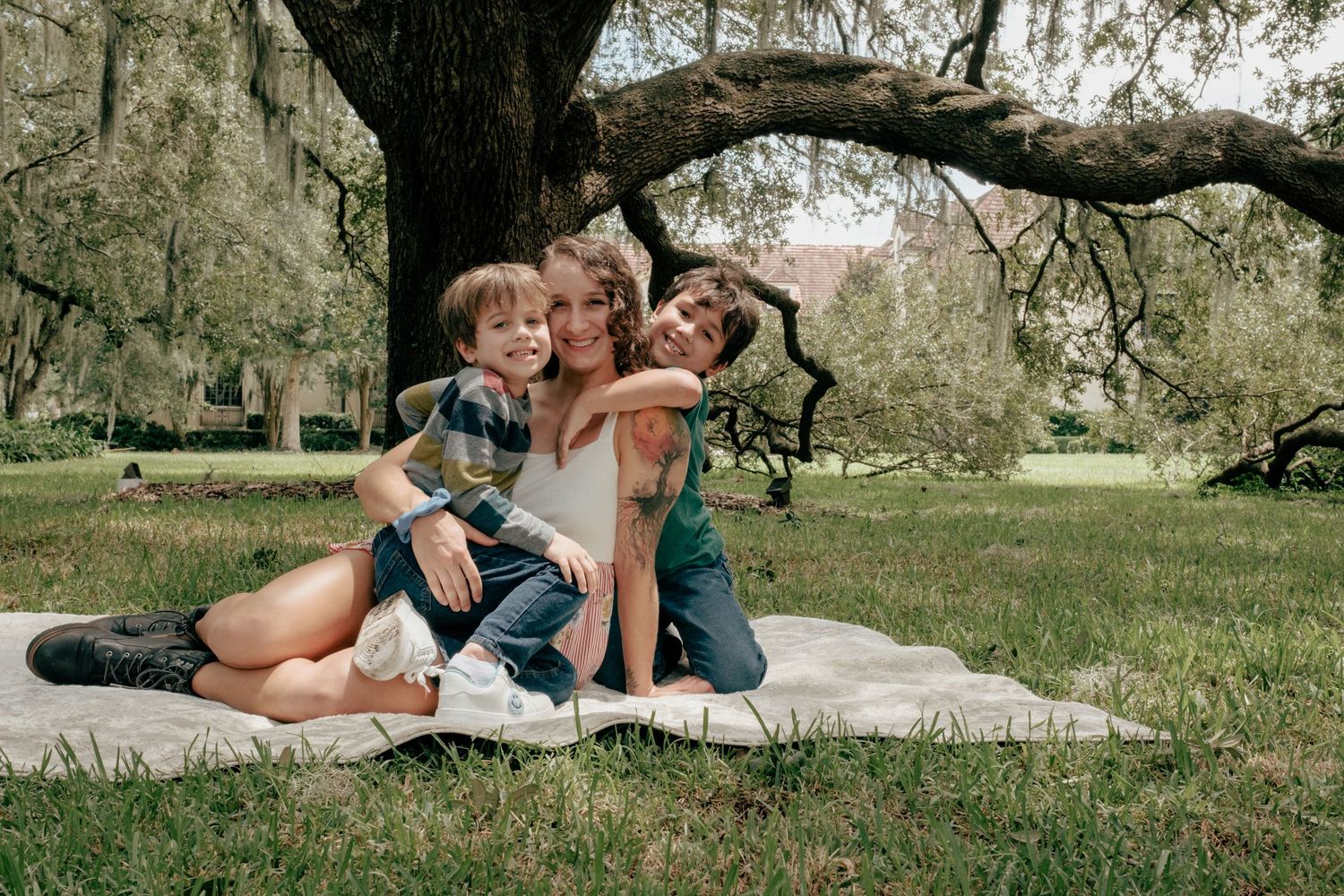 Couple sharing romantic moments together on blanket under large oak trees in a park setting.