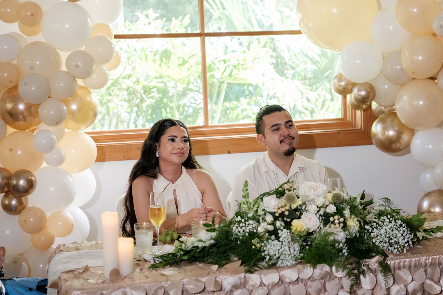 Wedding reception with white and gold balloon arch decorations and floral centerpieces.
