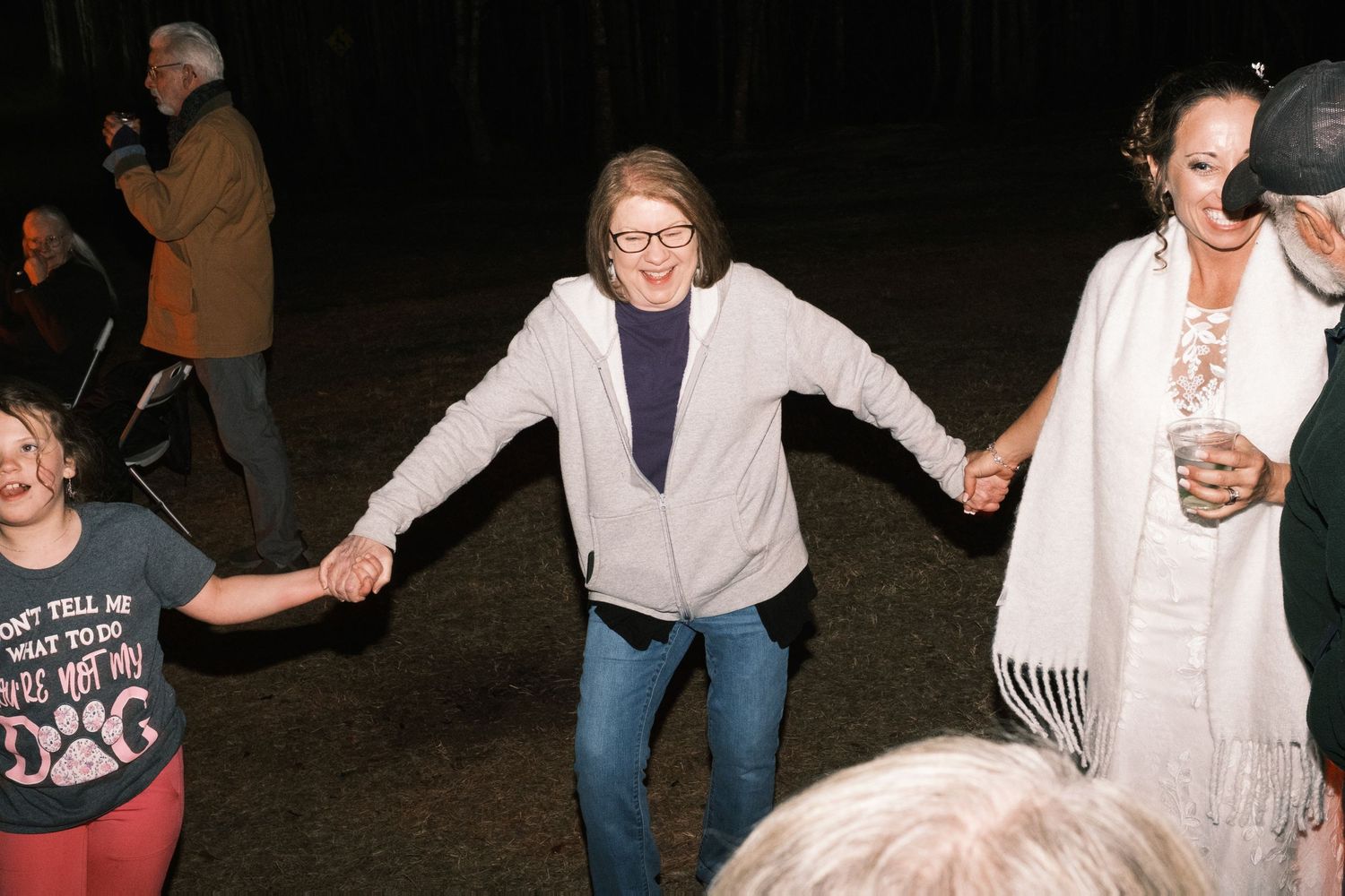 Women hold hands and dance together joyfully at an outdoor evening wedding reception.