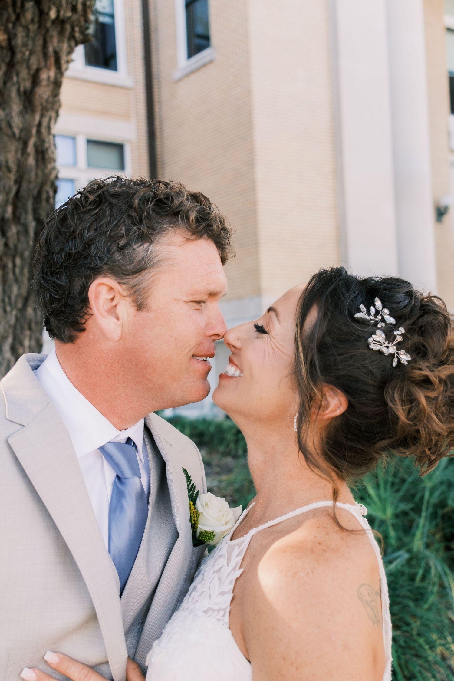 Bride and groom sharing a romantic almost-kiss near a tree outdoors.