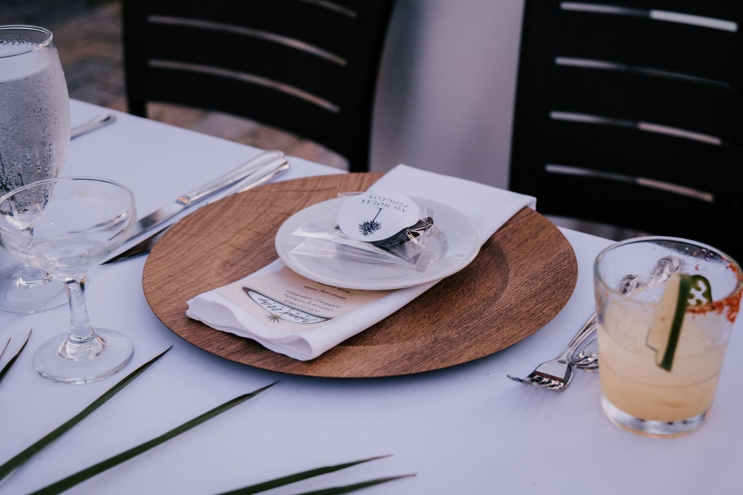Place settings with wooden chargers and white plates arranged on a dining table.