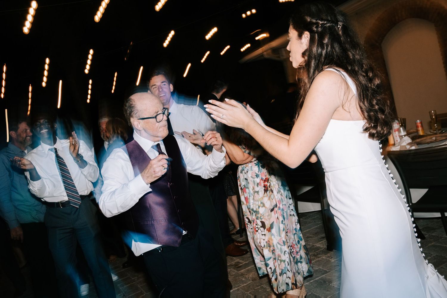 Wedding reception dance floor filled with guests celebrating under dimmed lighting.