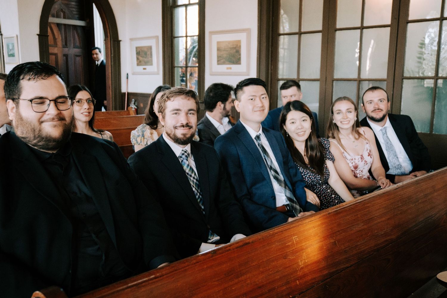 Wedding guests seated in wooden church pews during a ceremony.