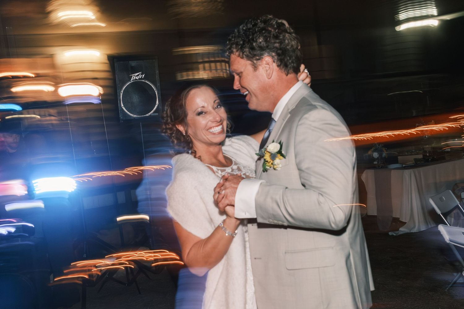 Bride and groom sharing joyful first dance at wedding reception with colorful lights.