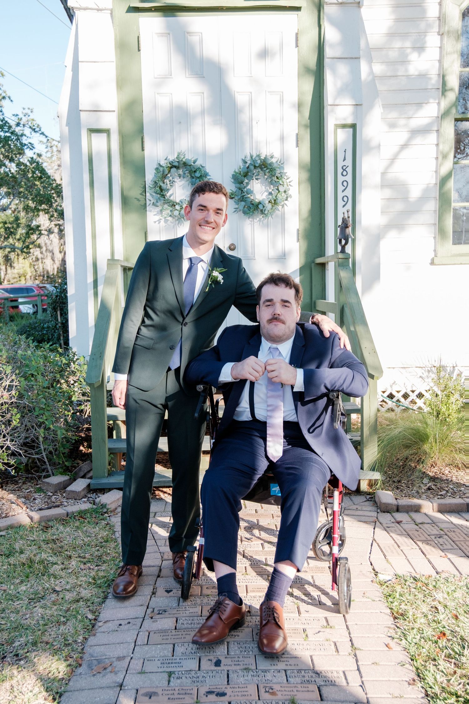 Groomsmen in suits pose playfully for a sequence of photos on a stone patio outside a white building.