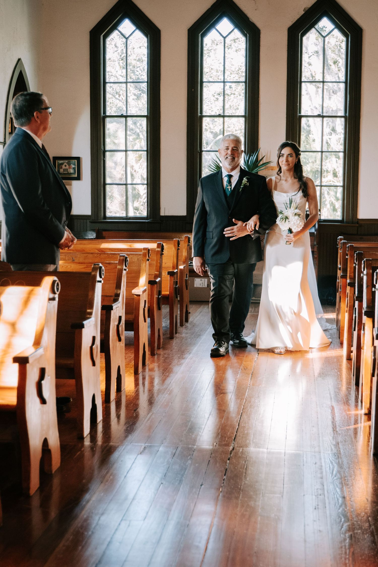 A wedding ceremony in a historic church with gothic arched windows and wooden pews.
