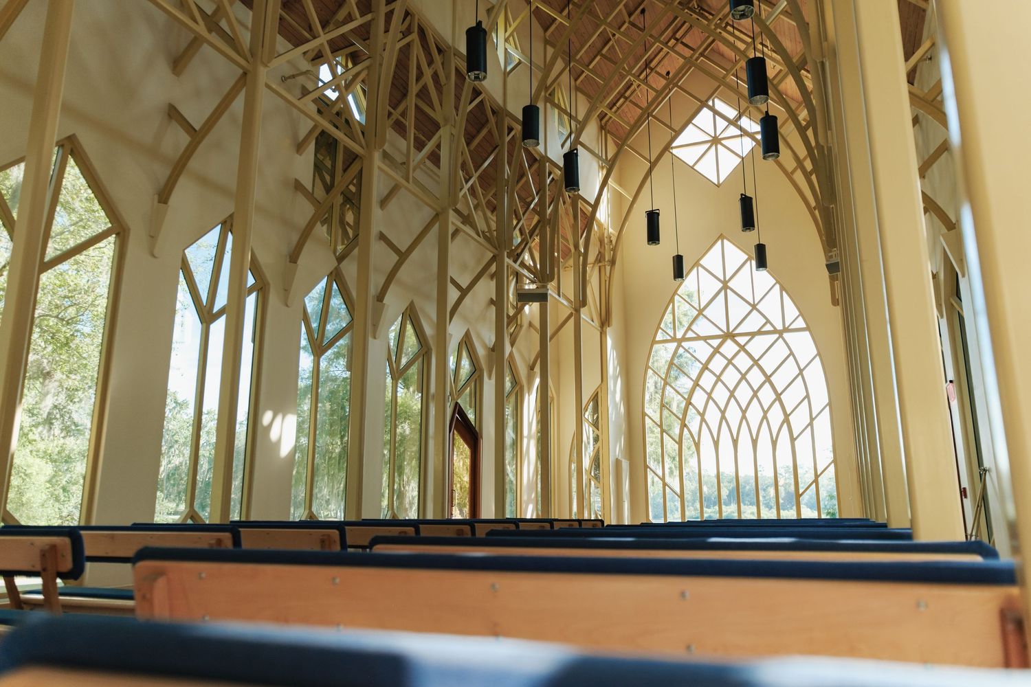 Empty chapel interior with wooden architectural details and dramatic pendant lighting leading to altar.