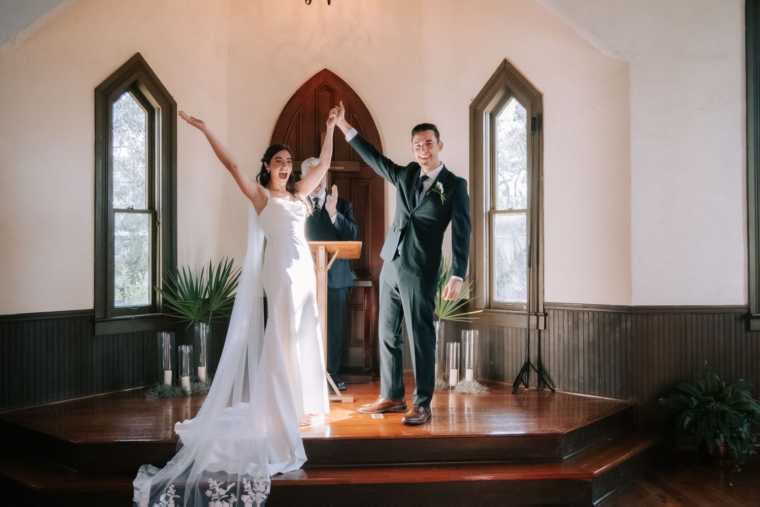 Interior of a chapel with Gothic arched windows and wooden floors during a wedding ceremony.
