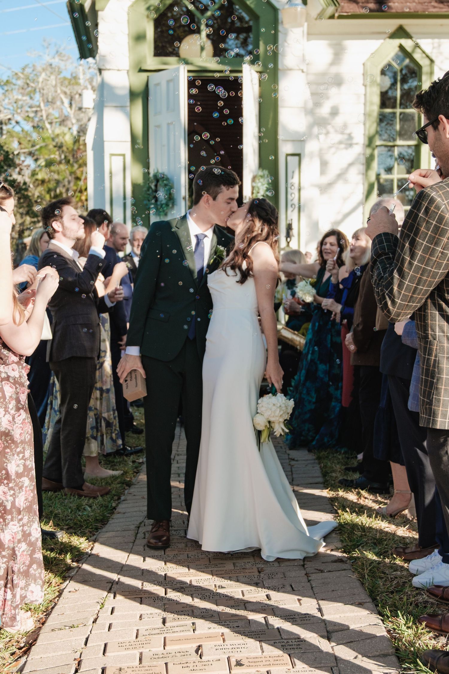 Wedding ceremony guests gathered outside white chapel in afternoon light.