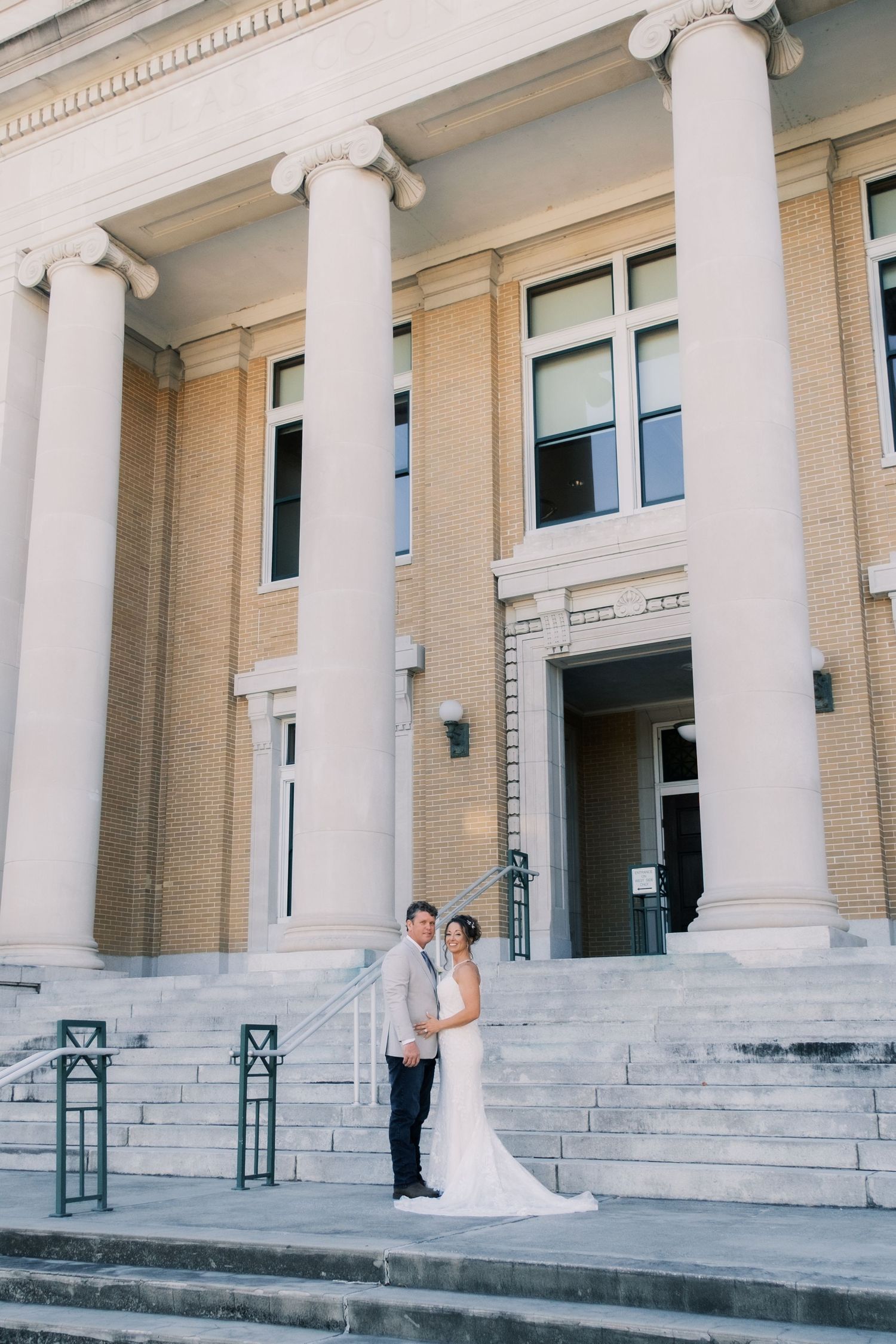 Bride and groom embracing on steps of grand neoclassical building with tall columns.