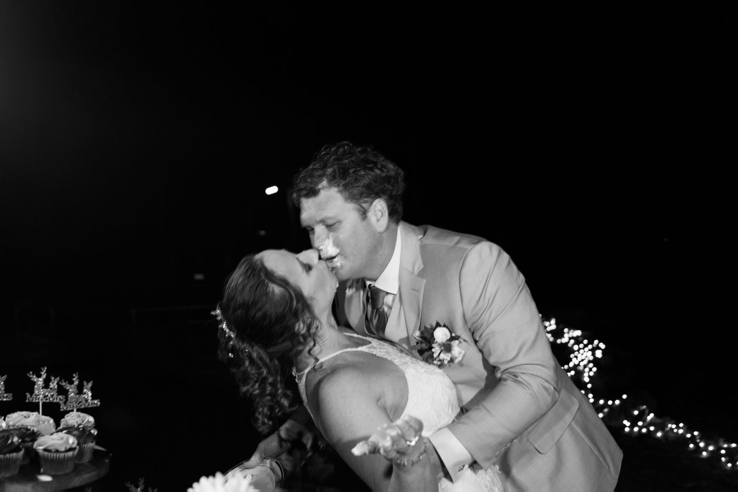 Black and white photo of bride and groom sharing a passionate dip kiss at their evening wedding reception.