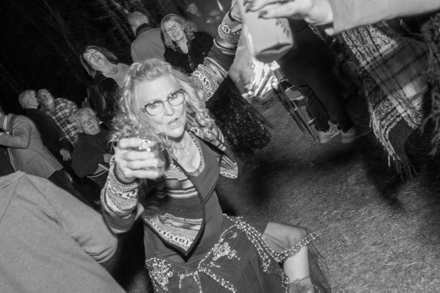 Black and white photo of a woman with glasses joyfully dancing at a wedding reception.