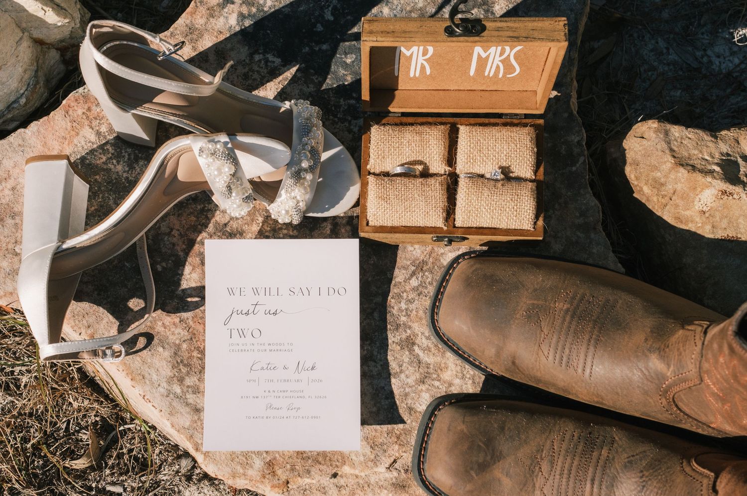 Wedding flat lay featuring bridal shoes, cowboy boots, rings, and elegant invitation suite.