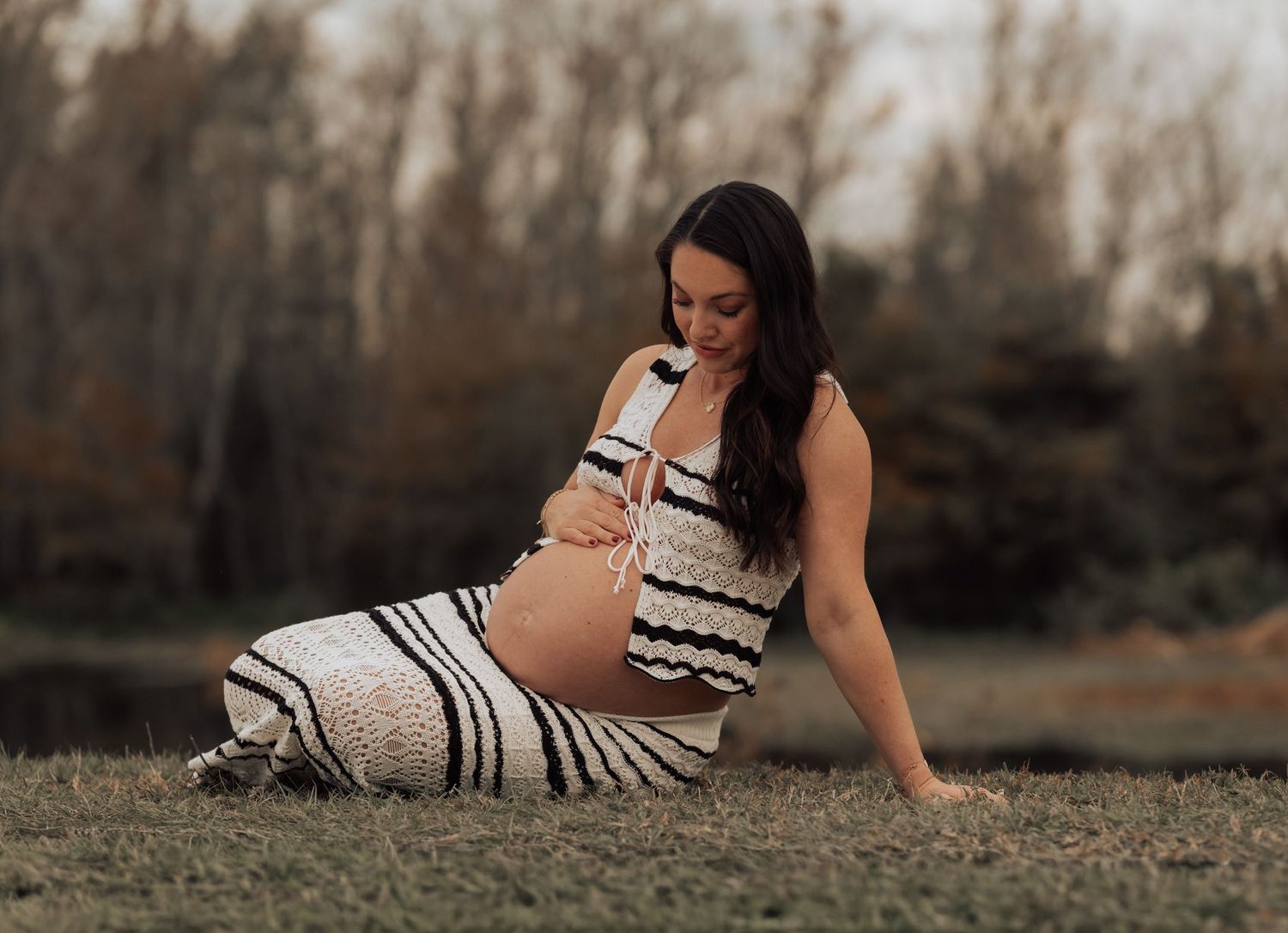 A person in a striped dress lies gracefully on grass during a moody outdoor photo session.