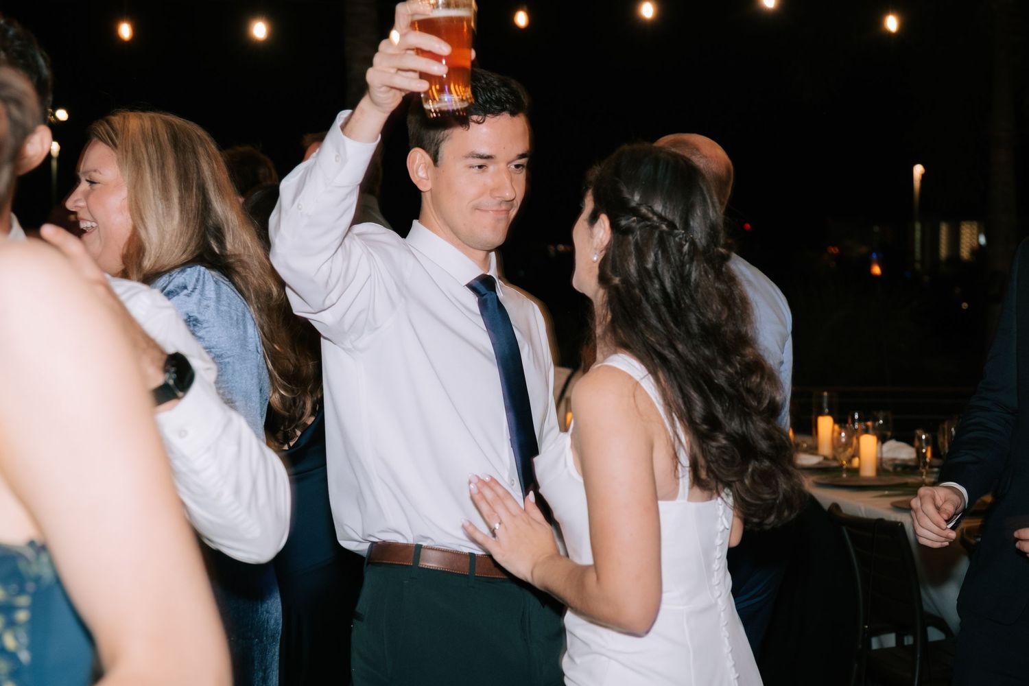 People dancing and socializing at a nighttime wedding reception with ambient lighting.