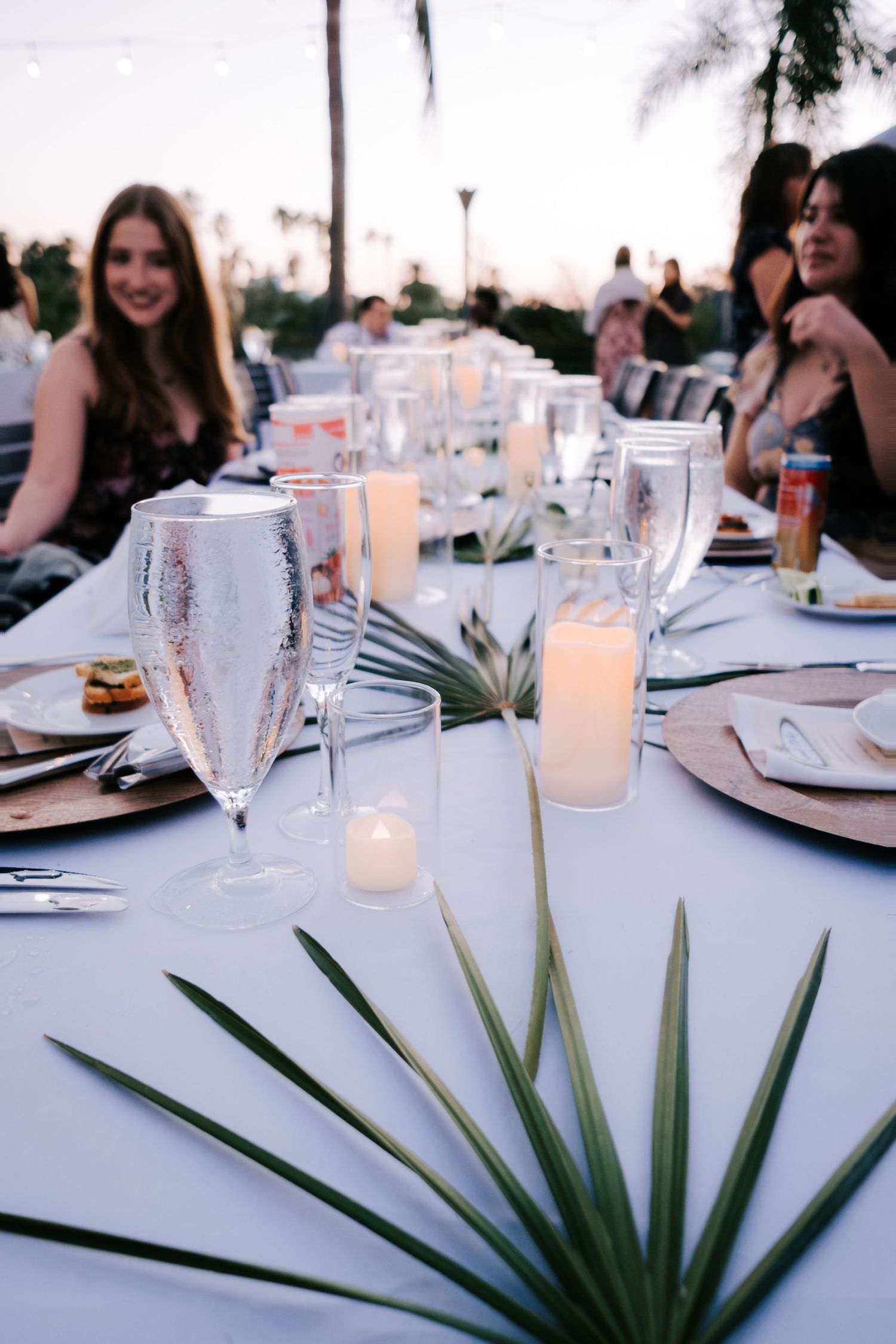 Elegant table setting with white linens, candles and tropical palm leaves as centerpieces.
