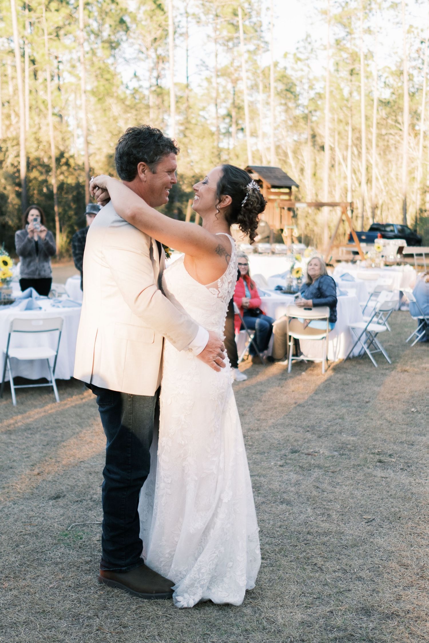 Bride and groom share first dance outdoors at sunset with wedding guests seated at tables.