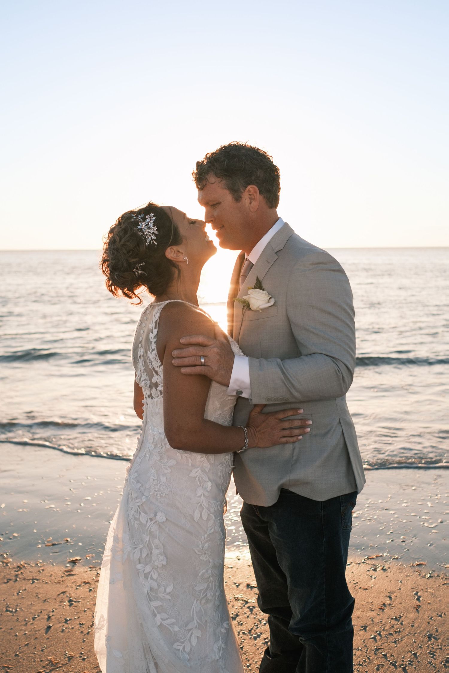 Bride and groom sharing romantic moment kissing on beach at golden sunset.