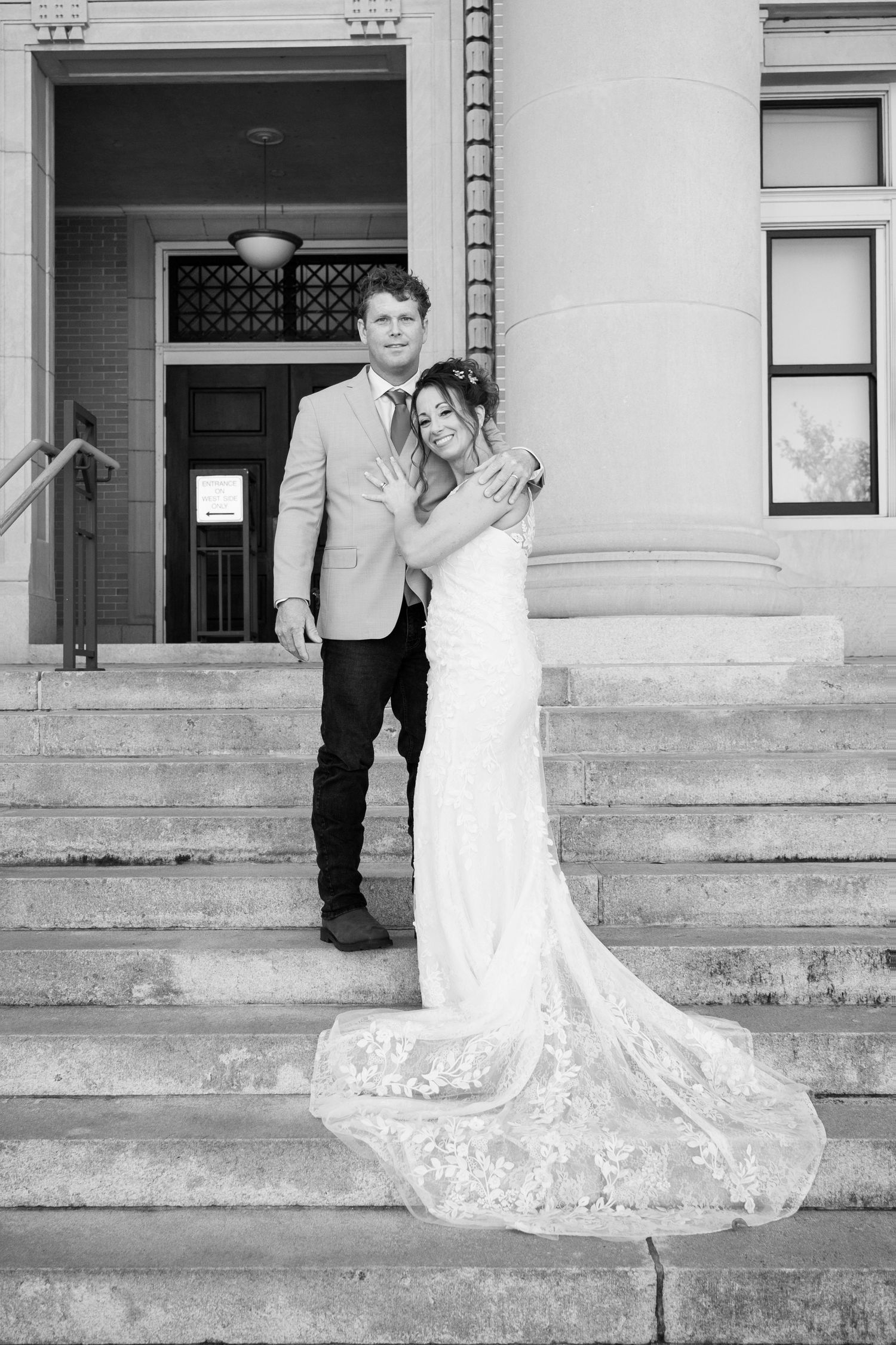 Black and white photo of bride and groom posing on stone steps of a classic building with columns.