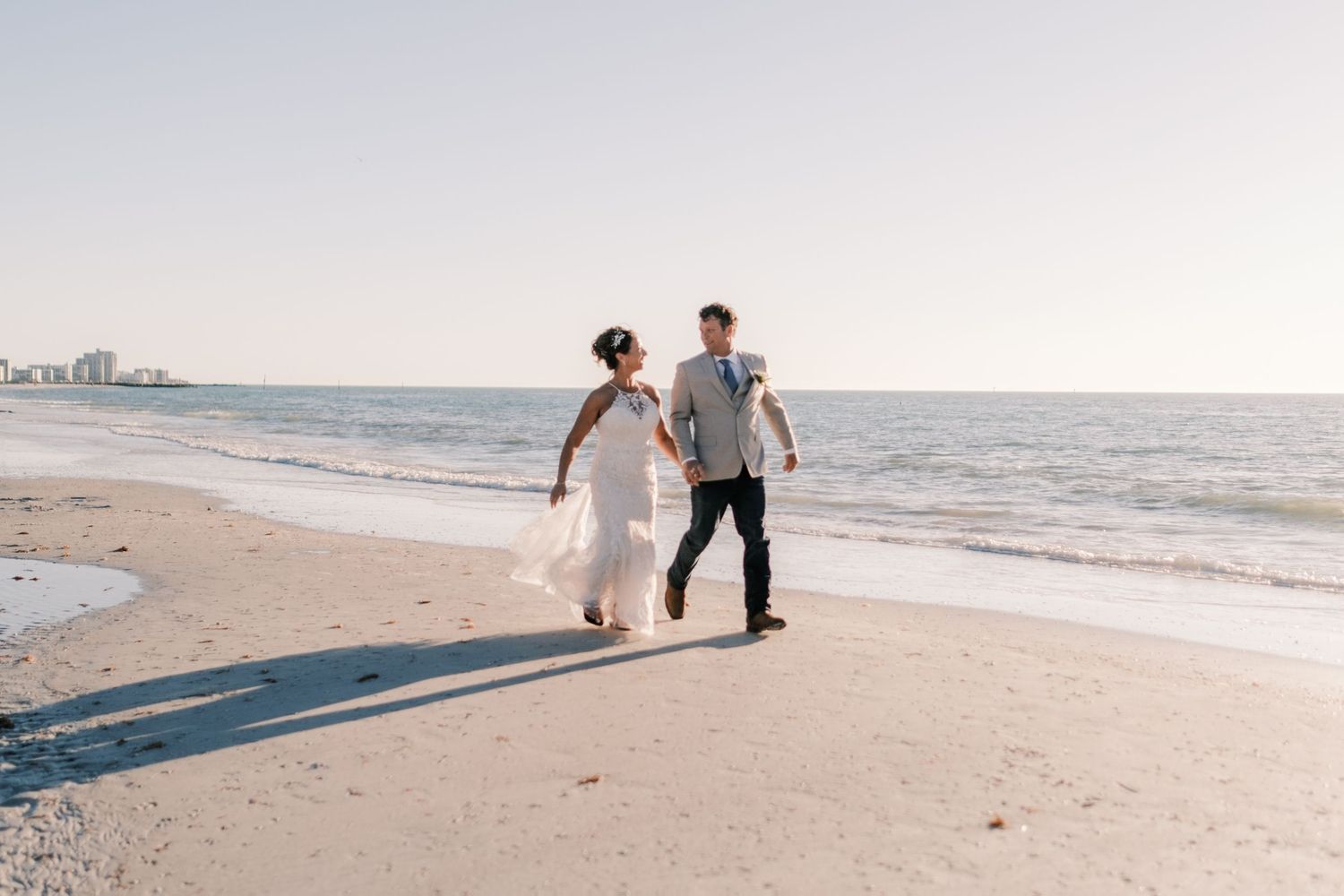 Bride and groom running hand in hand along a serene beach shoreline.