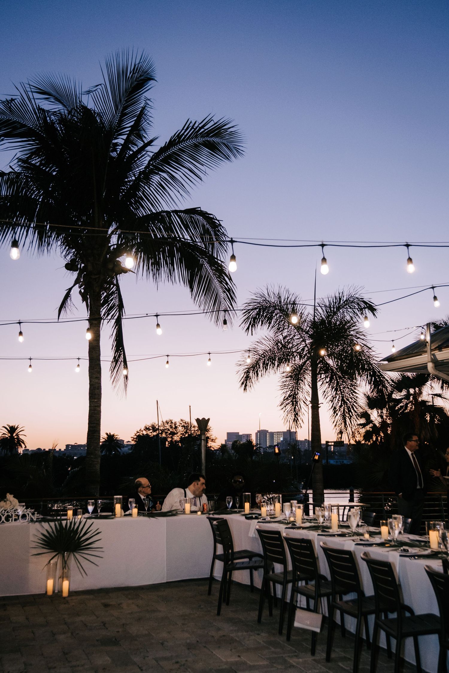 Tropical wedding venue at dusk with string lights and palm trees against a purple sky.